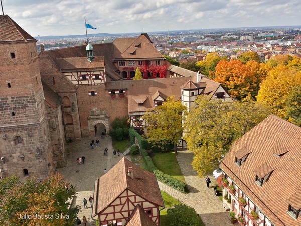 An aerial photograph captures Nuremberg Castle in autumn, with its historic buildings and colorful foliage overlooking the city.