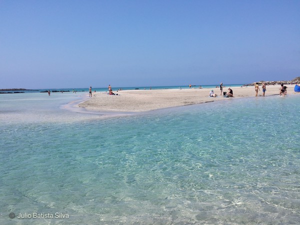 A scenic view of a narrow sandbar surrounded by clear turquoise water, with people enjoying the sunny day on the beach.