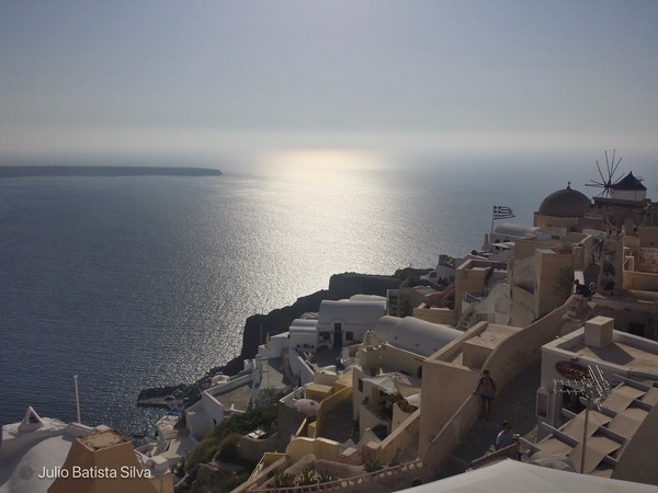 A scenic view of a Greek island village perched on a cliff overlooking the sparkling blue sea.