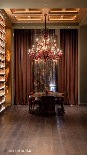 A dimly lit library features a large red chandelier, a round table, and a bookshelf.